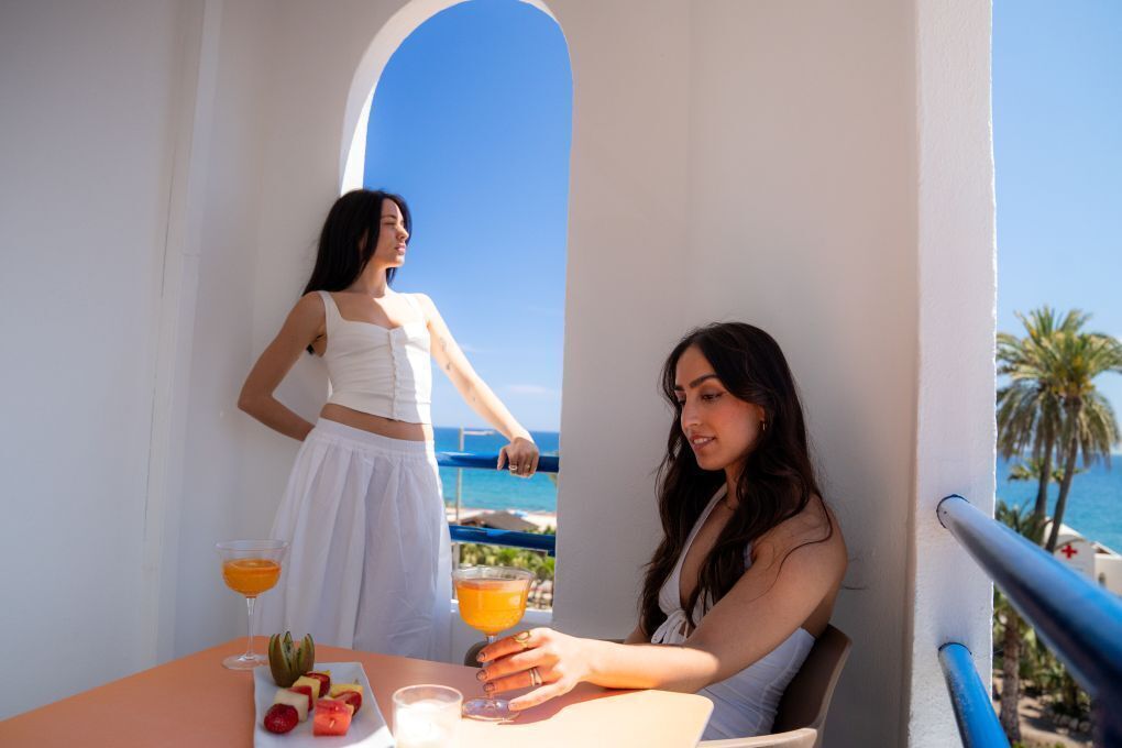 Dos personas en una mesa con bebidas y fruta, con vistas a la costa.