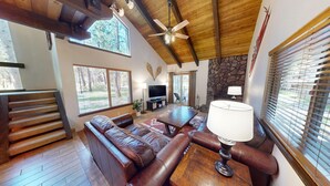 A spacious living area with a leather sofa, a wooden coffee table, a television, and a stone fireplace. - Spa-Side Lodge with Access to Exclusive Golf (Sunriver)