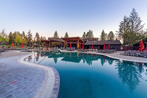 A swimming pool with lounge chairs and umbrellas, surrounded by trees and a wooden building.