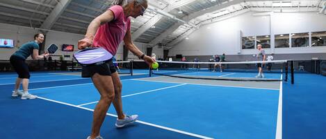 Een indoor tennisbaan met een hoge nok, een net en meerdere spelers.