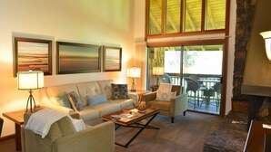 A cozy living room with a sofa, armchairs, a coffee table, and a fireplace. There are large windows and a view of the outdoors. - Sunriver Stay with Access to The Cove (Sunriver)