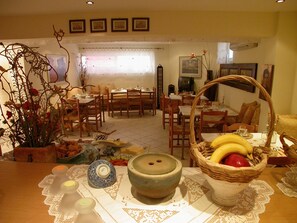 A dining area with multiple tables and chairs, a large vase with flowers, and a basket of fruit.