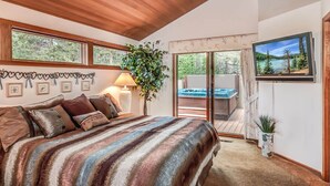 A bedroom with a large bed, a sliding glass door leading to a hot tub, and a TV mounted on the wall. - Family Golf Escape with Access to The Cove (Sunriver)