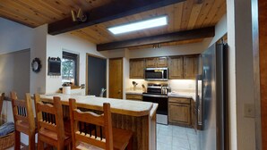 Una cocina con armarios de madera, un refrigerador de acero inoxidable, un microondas y una estufa. Hay una mesa de comedor con sillas de madera.