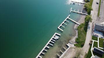 An aerial view of a waterfront property with a dock extending into the water, a parking lot, and a building with a sloped roof.