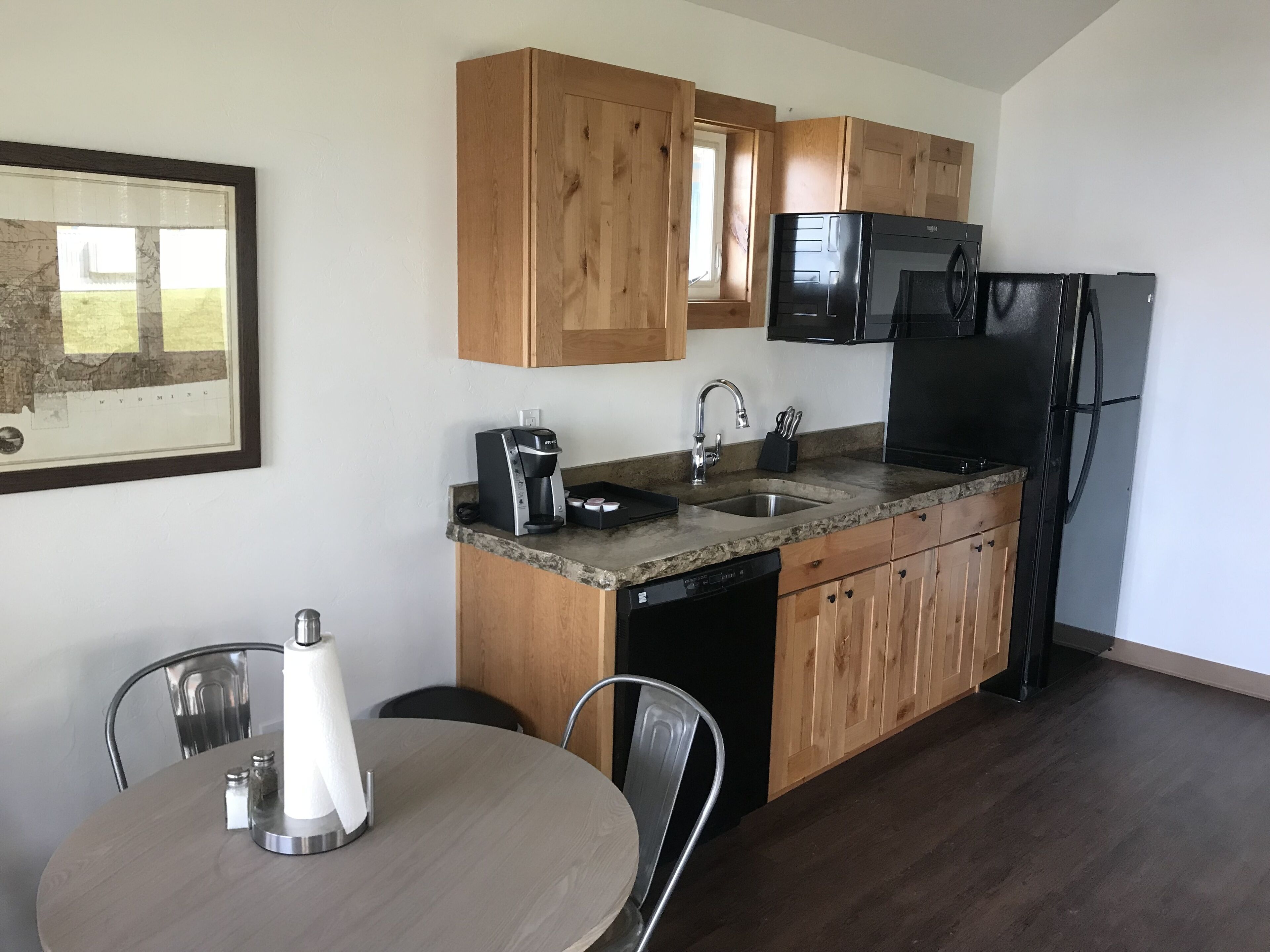 A compact kitchen with wooden cabinets, a black refrigerator, a microwave, and a coffee maker.