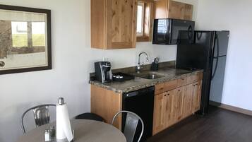 A compact kitchen with wooden cabinets, a black refrigerator, a microwave, and a coffee maker.