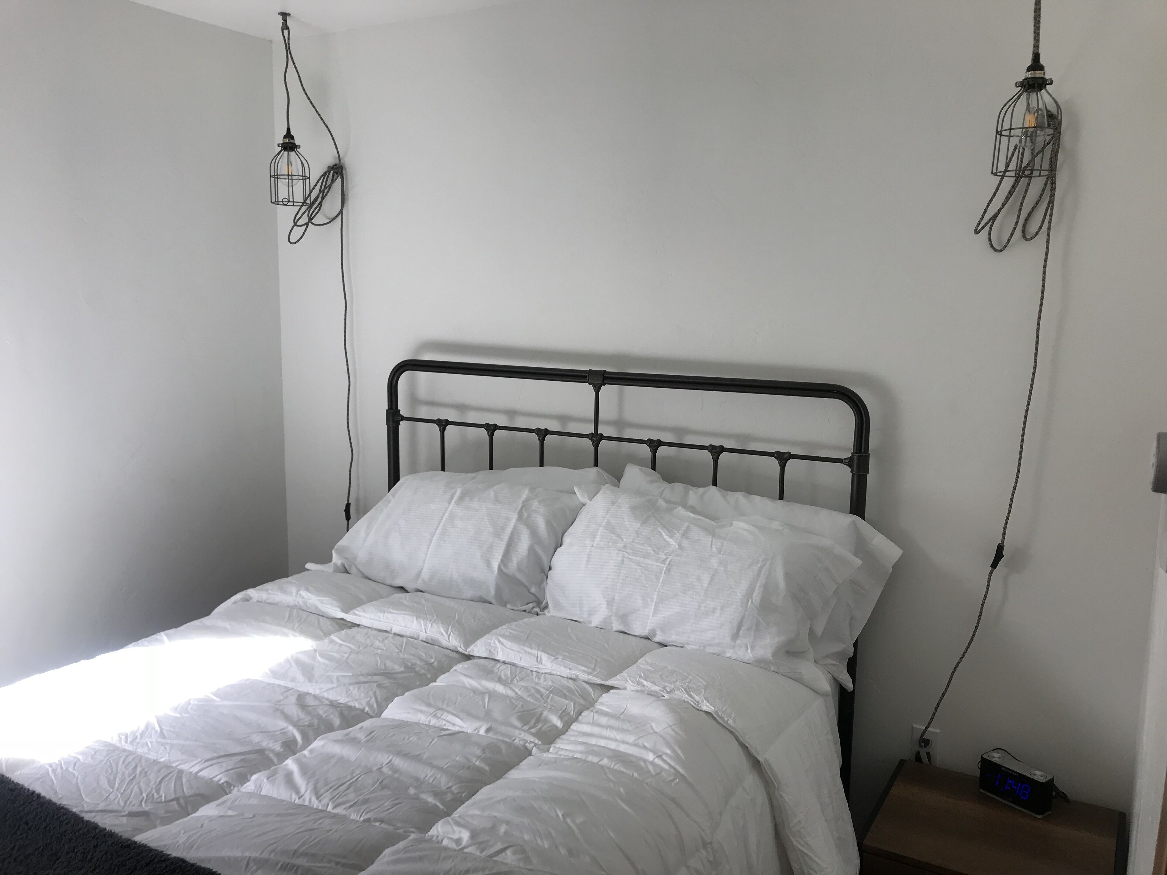 A bed with white bedding, a metal headboard, and two hanging light fixtures.
