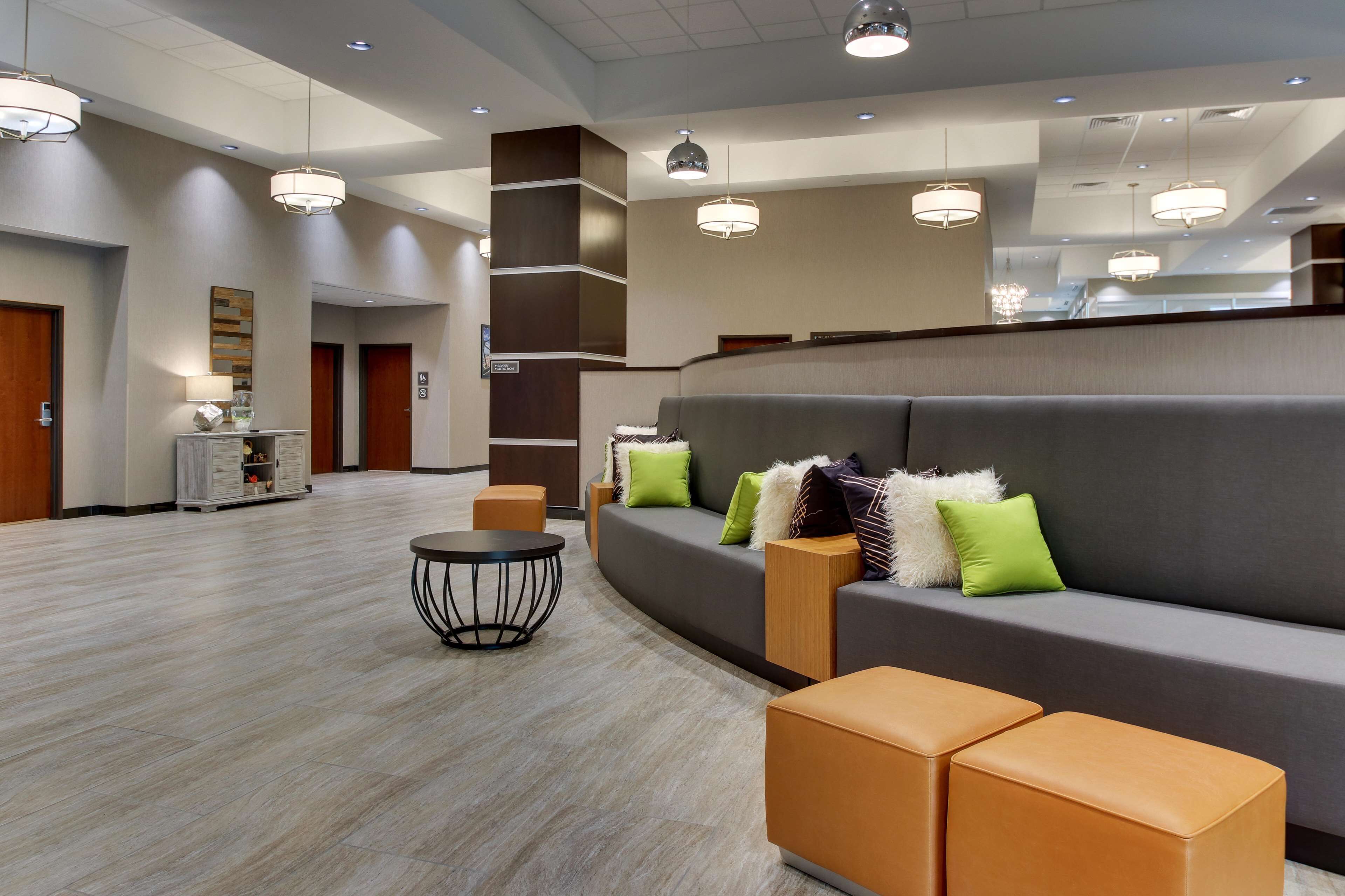 A modern lobby with a curved gray sofa, orange ottomans, a round black table, and multiple pendant lights.