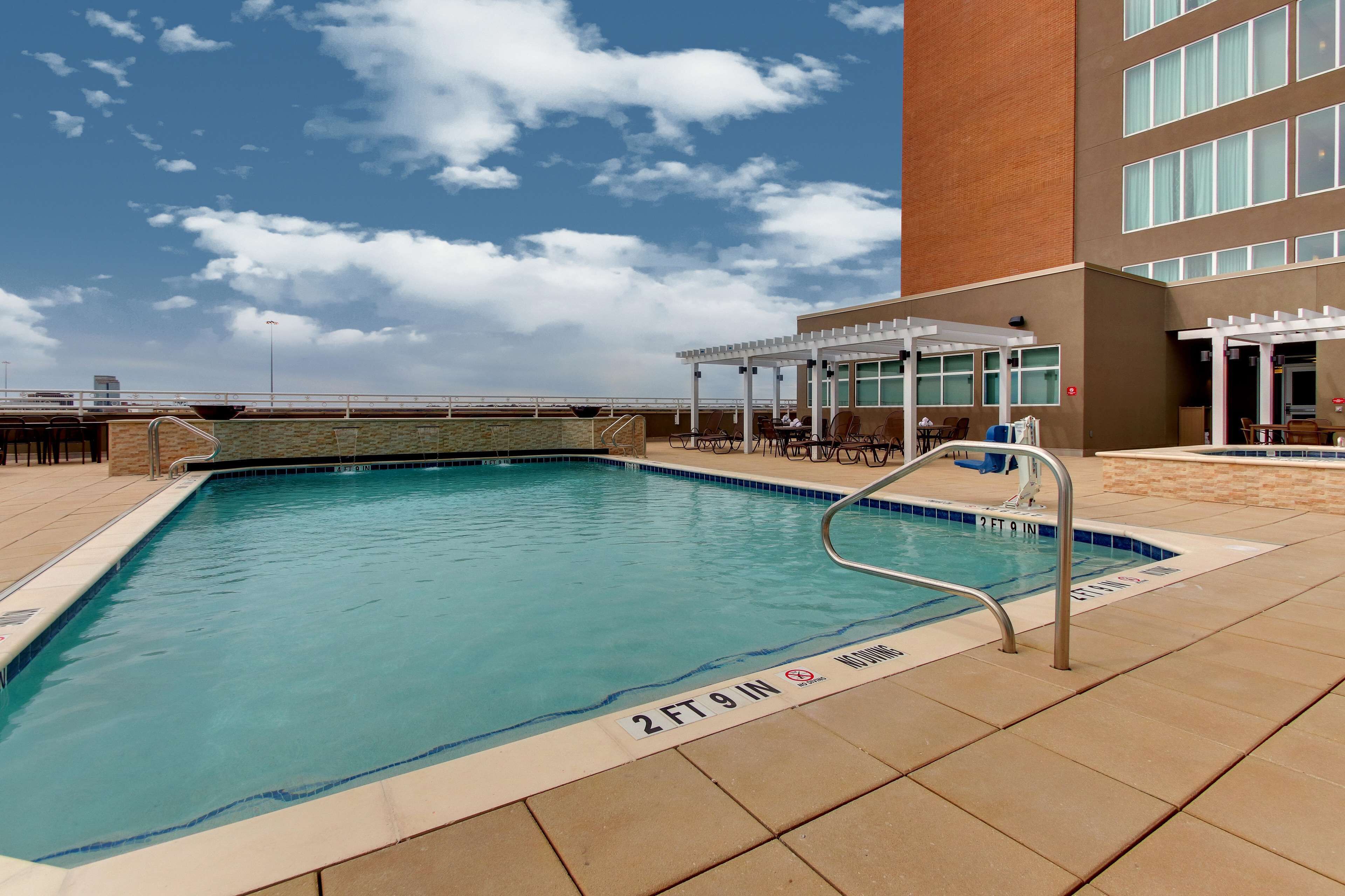 Une piscine dont la profondeur est indiquée à 2 pieds et 9 pouces, entourée d’un espace de repos couvert avec des tables et des chaises.