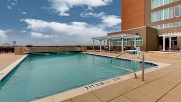 Une piscine dont la profondeur est indiquée à 2 pieds et 9 pouces, entourée d’un espace de repos couvert avec des tables et des chaises.