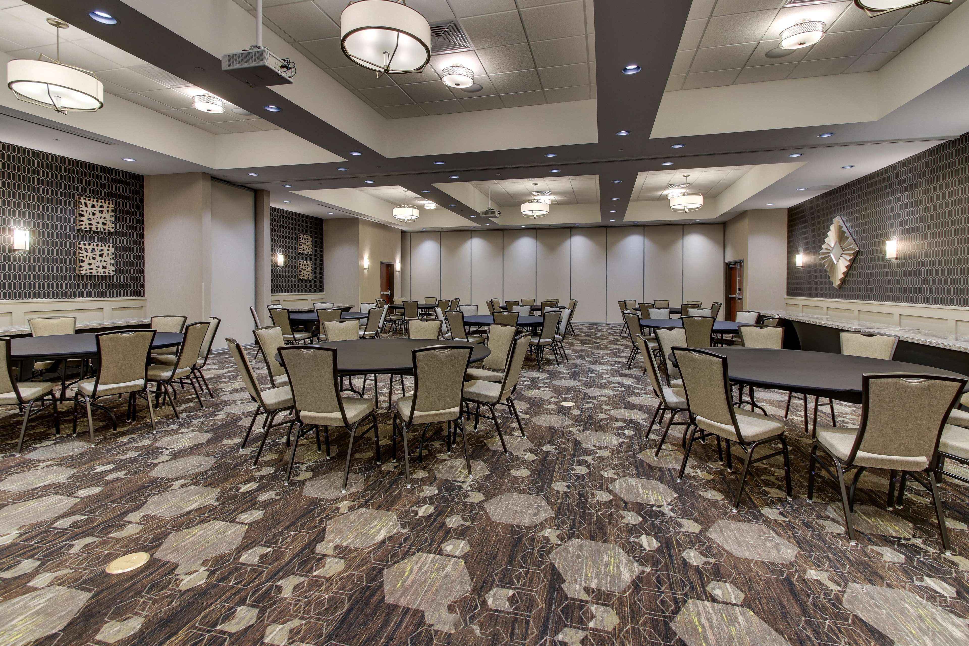 A conference room with multiple tables and chairs, a patterned carpet, and recessed lighting.