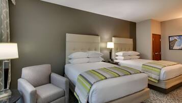 Una habitación de hotel con dos camas, una silla, una lámpara y un cuadro en la pared.