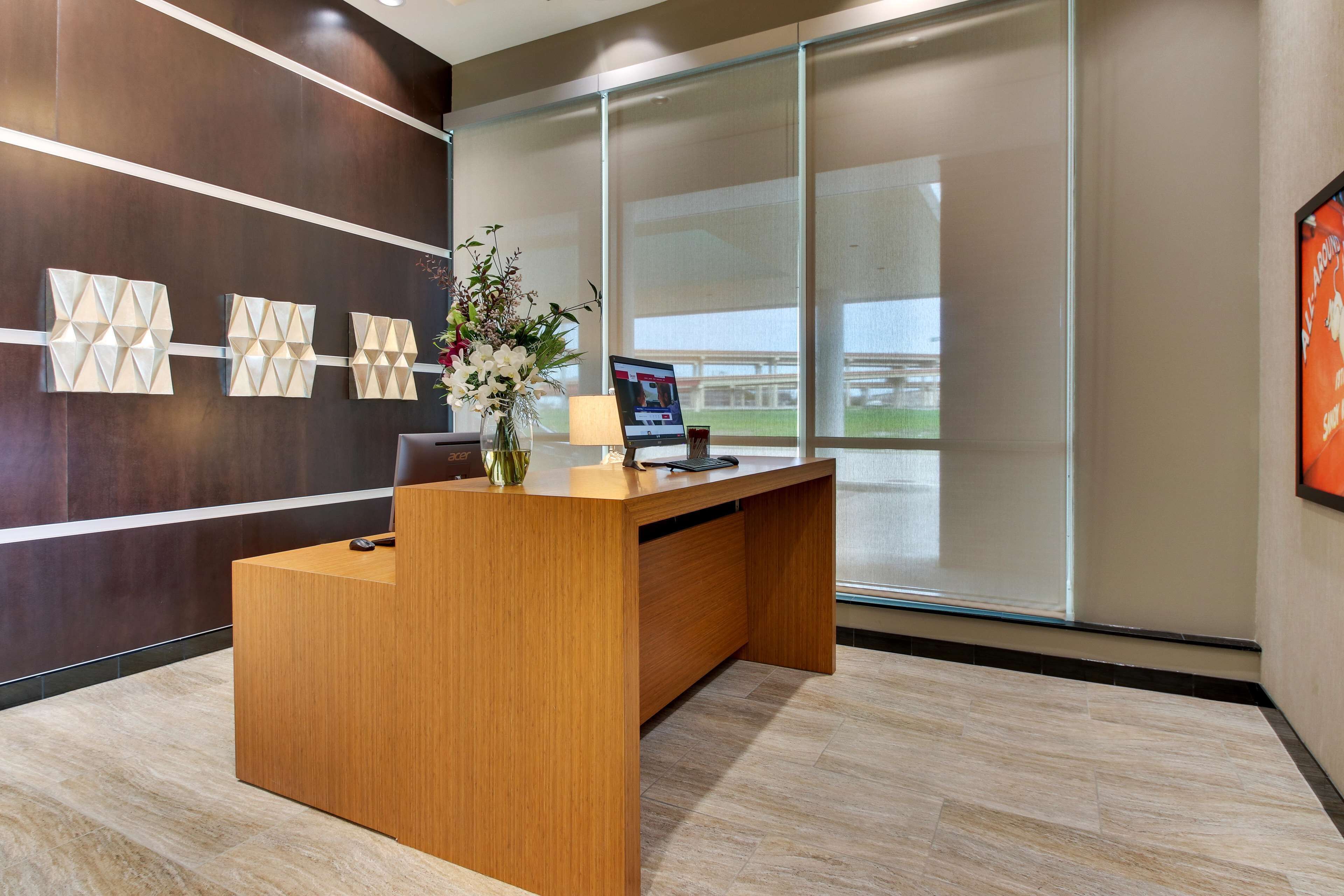 A modern reception desk with a wooden finish, a vase with flowers, a laptop, and a framed picture on the wall.