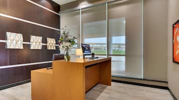A modern reception desk with a wooden finish, a vase with flowers, a laptop, and a framed picture on the wall.