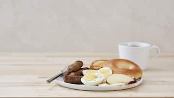 Un plato con un bagel, huevos duros en rodajas, salchichas y rodajas de manzana sobre una mesa de madera.