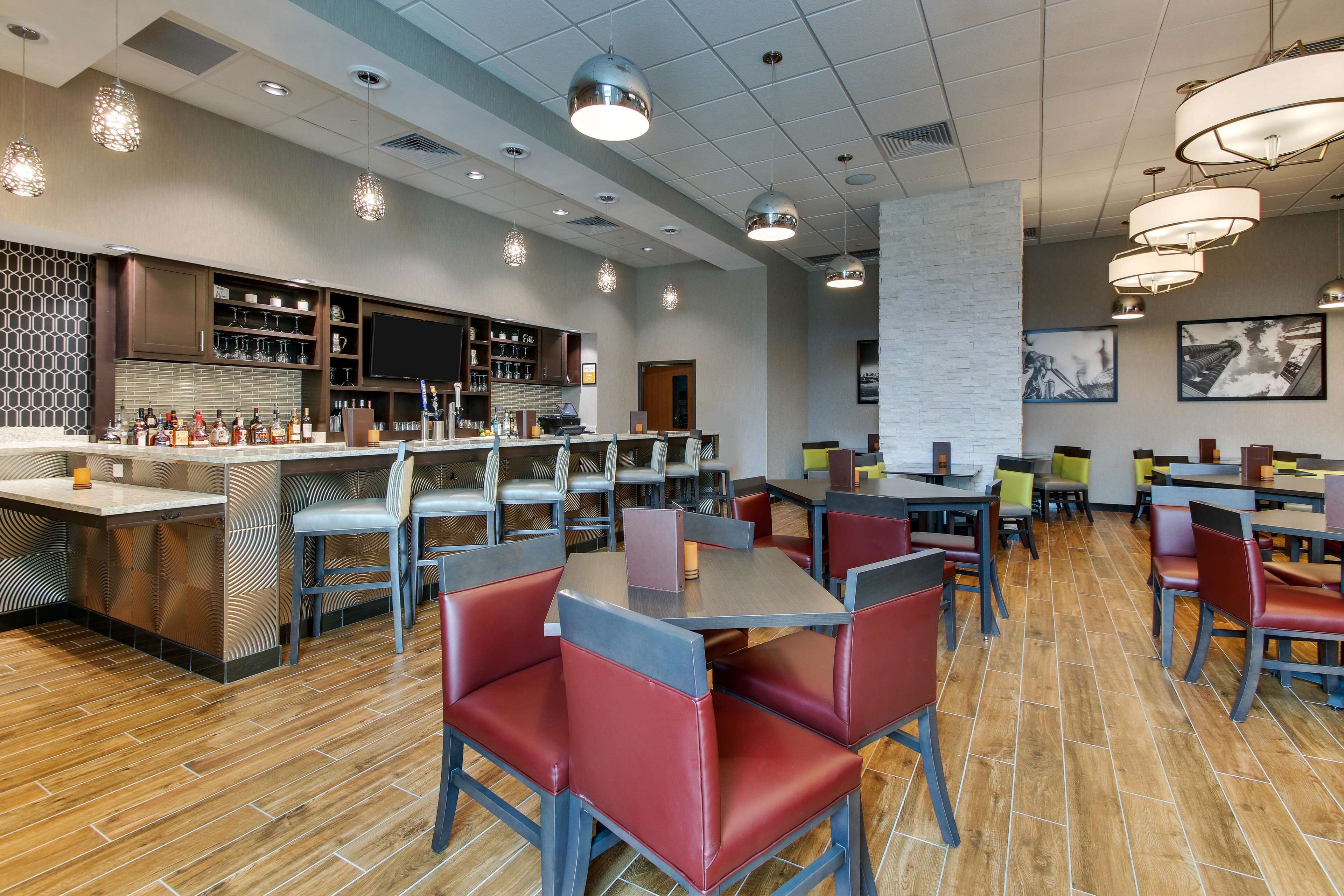 A modern restaurant with a bar area, wooden flooring, and red upholstered booths.