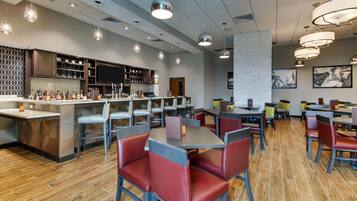 A modern restaurant with a bar area, wooden flooring, and red upholstered booths.