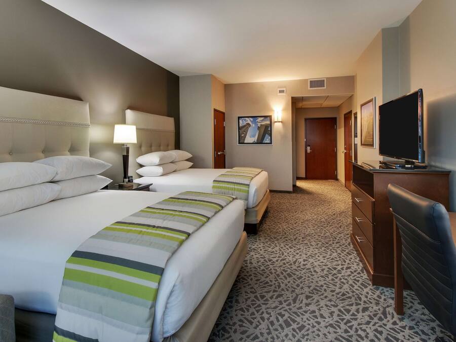 A hotel room with two beds, a desk, a television, and a patterned carpet.