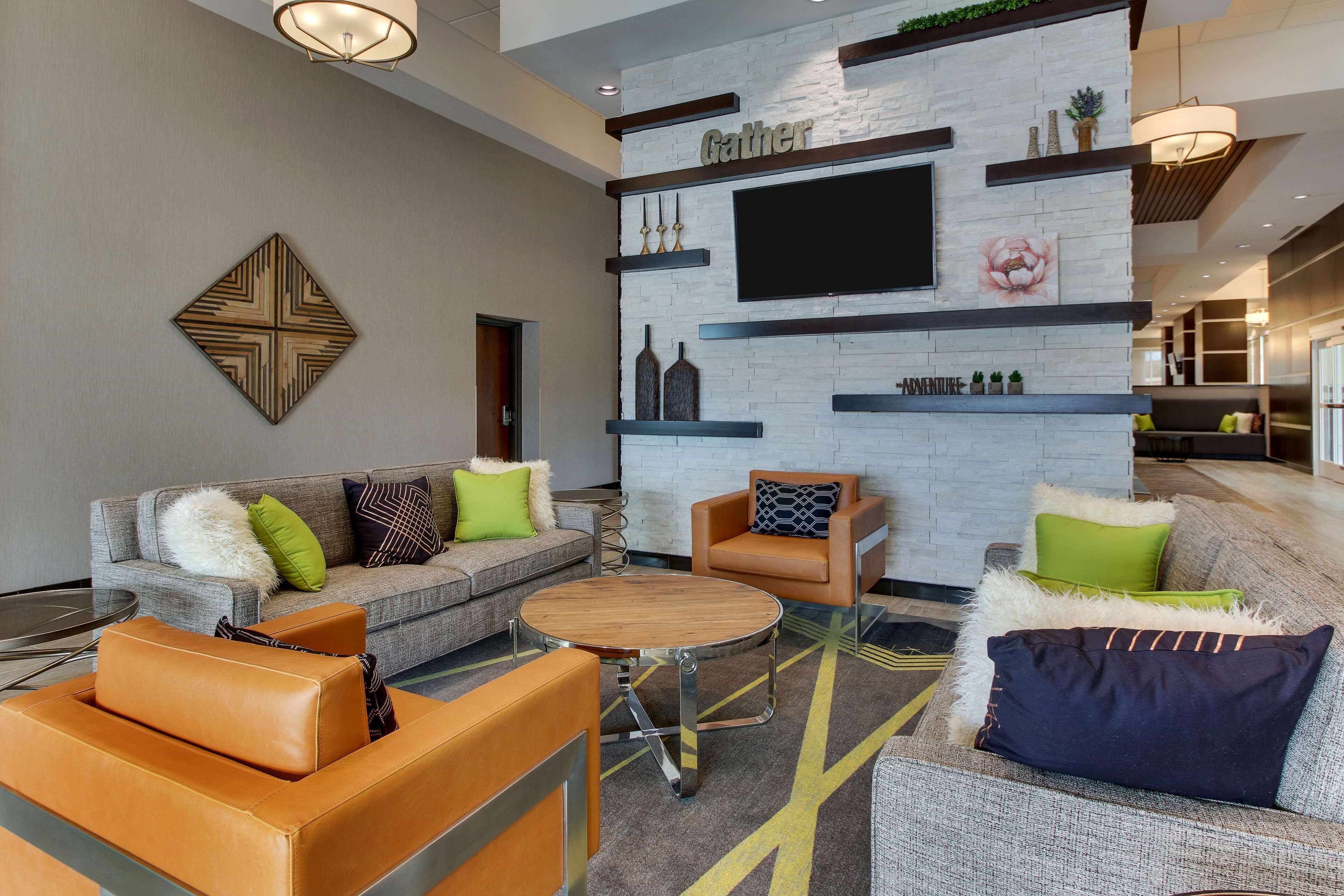 Un'area lounge moderna con un divano, poltrone e un tavolino. Un televisore a schermo piatto è montato a parete, e sono presenti elementi decorativi e un camino.