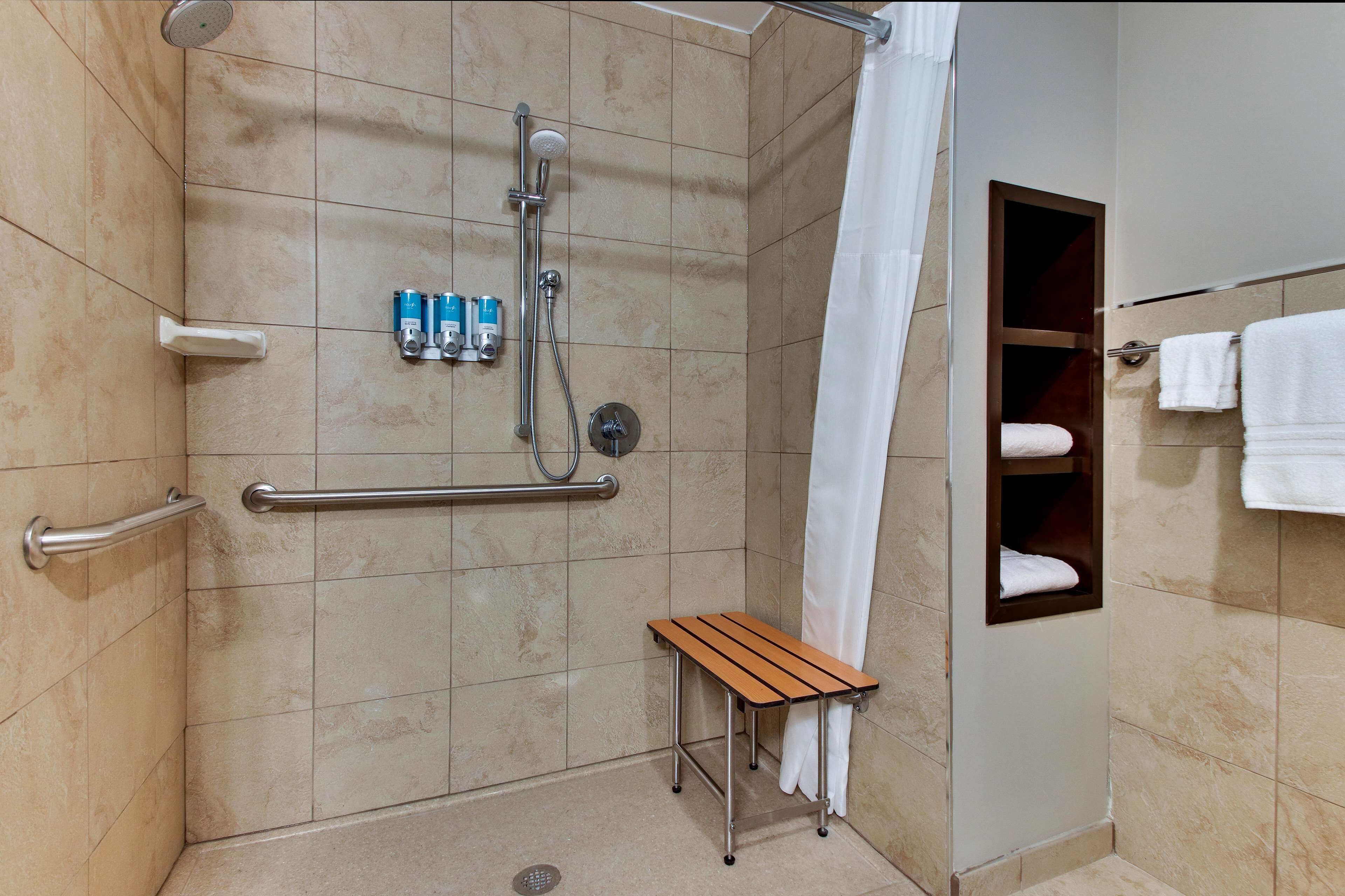 A shower area with a handheld showerhead, grab bars, a bench, and a towel rack.