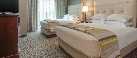 A hotel room with two beds, a television, a lamp, and a patterned carpet.
