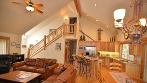 A spacious living area with a high ceiling, a wooden staircase, a kitchen with wooden cabinets, and a dining area with a table and chairs. - Sunriver Escape with Access to The Cove (Sunriver)