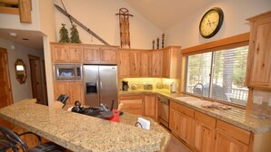 A kitchen with wooden cabinets, granite countertops, a stainless steel refrigerator, a coffee maker, and a clock on the wall. - Sunriver Escape with Access to The Cove (Sunriver)