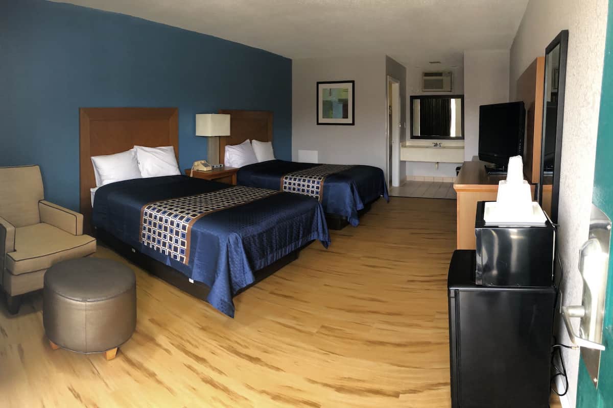 Quarto de hotel com duas camas, uma escrivaninha, uma cadeira, uma lixeira e uma televisão.