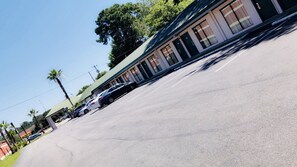 A parking lot with a row of buildings, including a motel with a green roof and striped curtains.