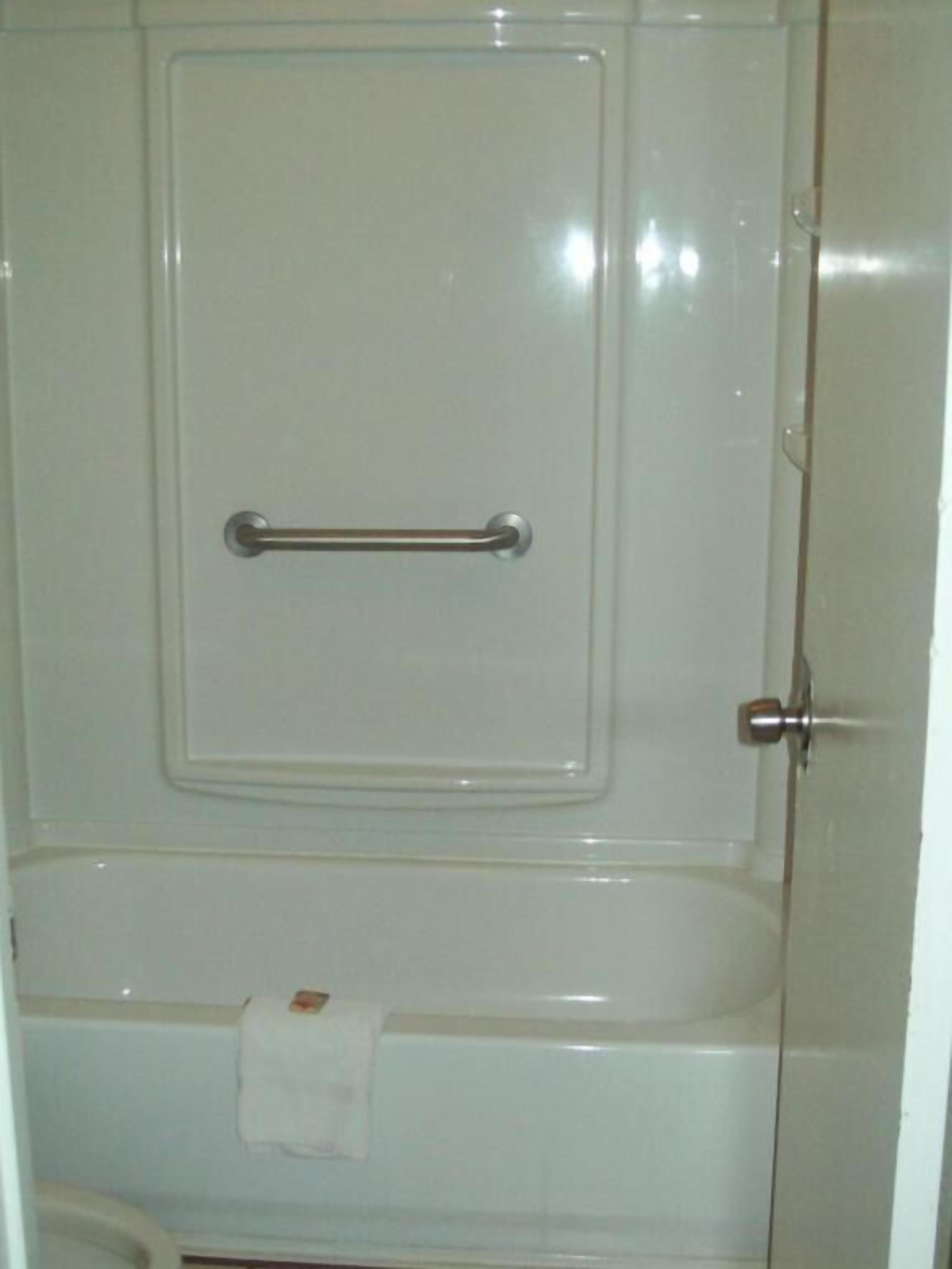 A bathroom with a white bathtub, a towel hanging on the side, and a grab bar installed on the tub.