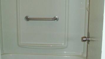 A bathroom with a white bathtub, a towel hanging on the side, and a grab bar installed on the tub.