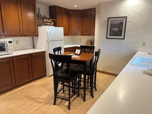 A kitchen with wooden cabinets, a white refrigerator, a dining table with four chairs, and a white countertop. - Calm River Oasis with Access to The Cove (Sunriver)