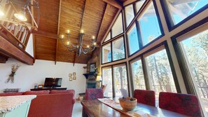 A spacious room with a wooden ceiling, large windows, a fireplace, and a dining area.
