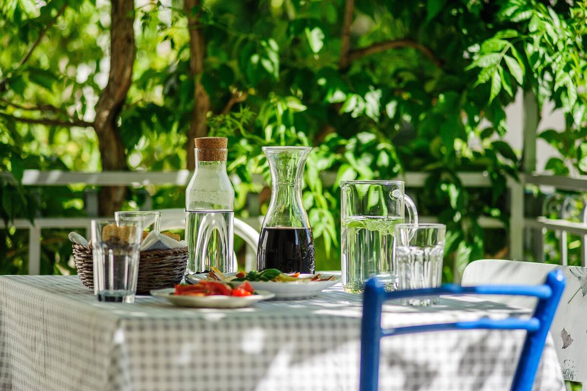 A table set outdoors with various glass containers and plates, surrounded by lush greenery.