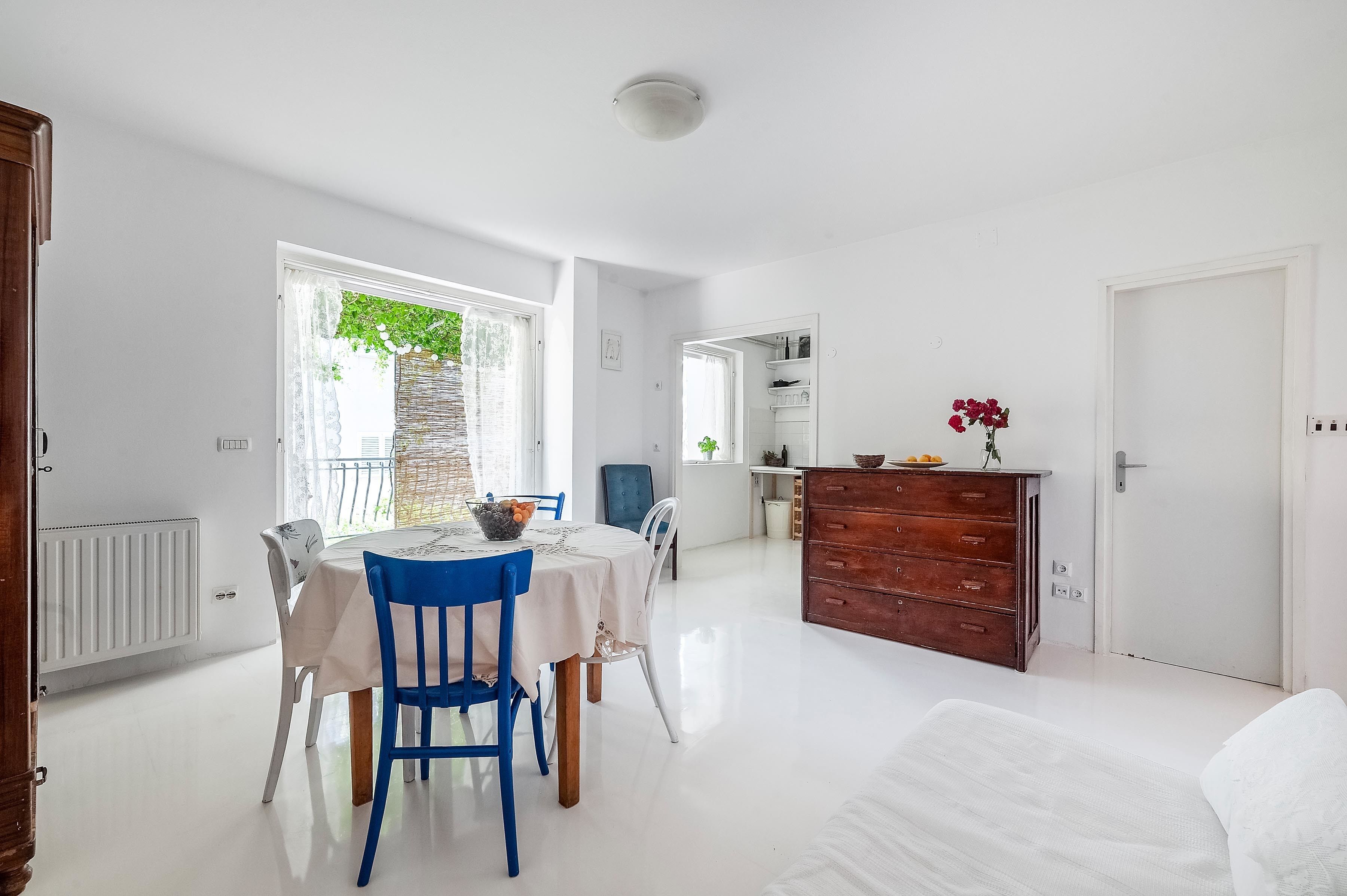 A bright, spacious room with a dining table, chairs, a dresser, and a bed.