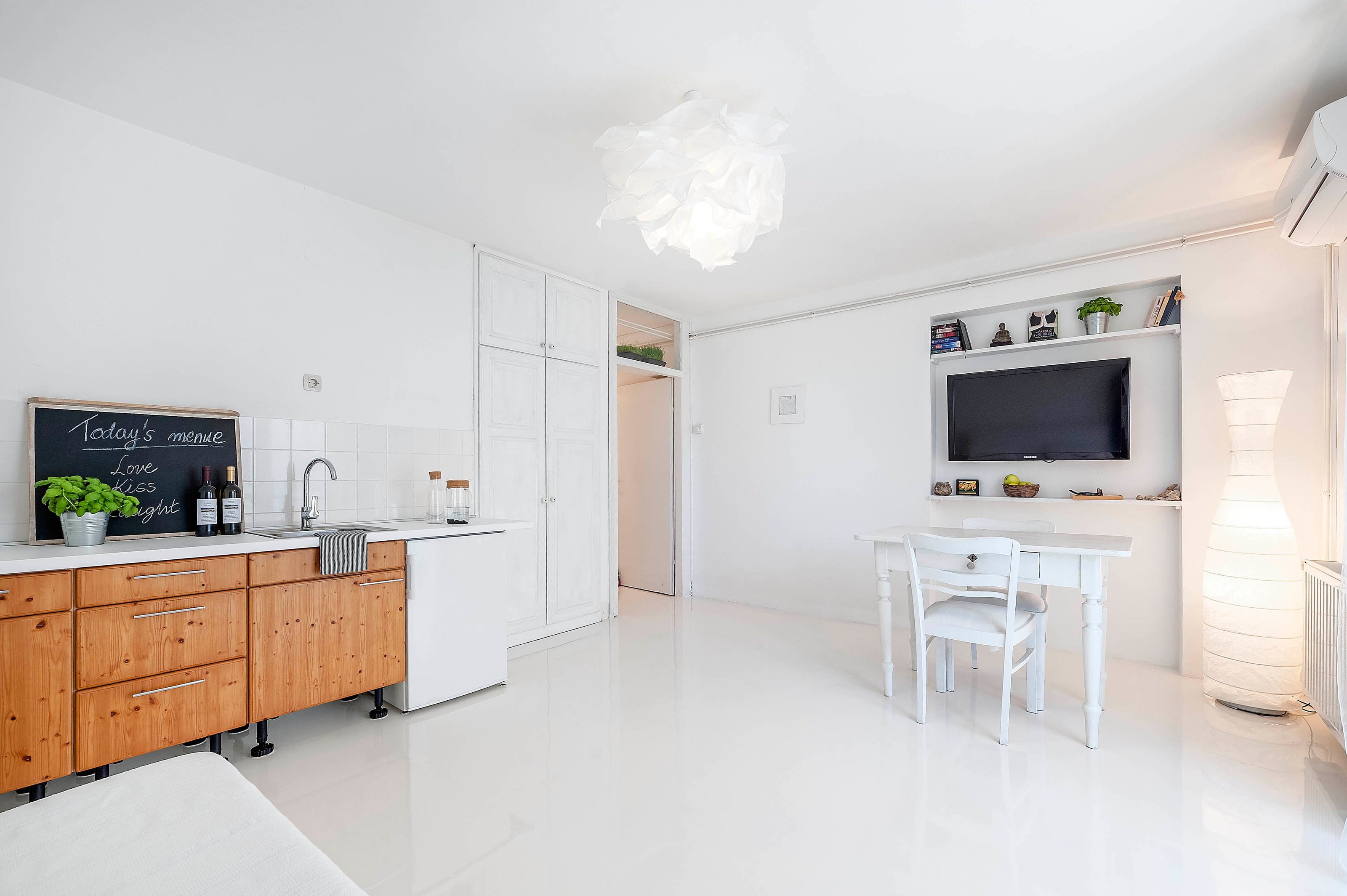Een moderne keuken met witte kasten, een krijtbordmenu en een eethoek met een witte tafel en stoelen.