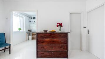 Una cocina moderna con paredes blancas, un aparador de madera, una silla azul y un jarrón con flores rojas en la encimera.