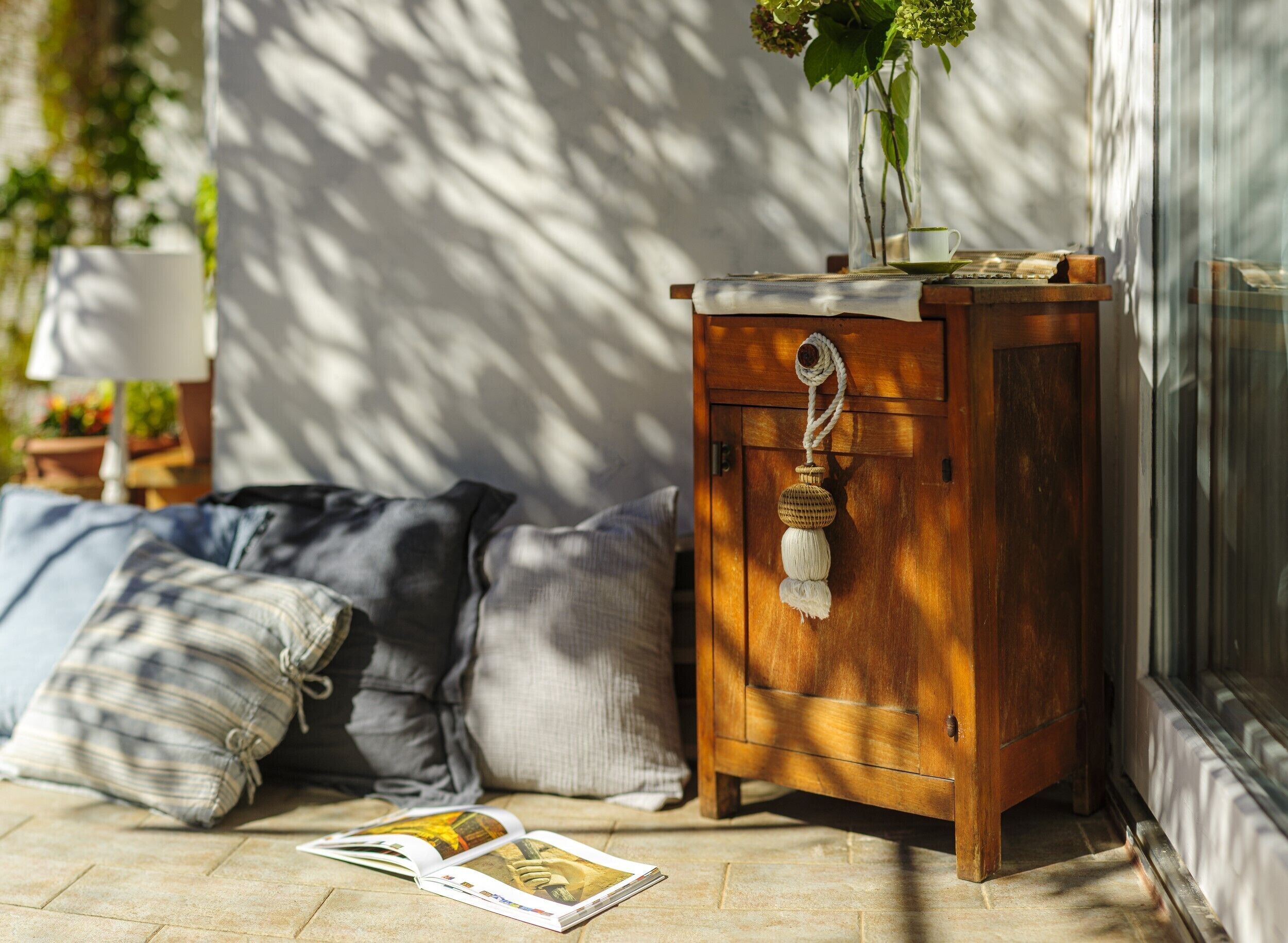 A wooden cabinet with a rope handle, a cushion, and a magazine on the floor.
