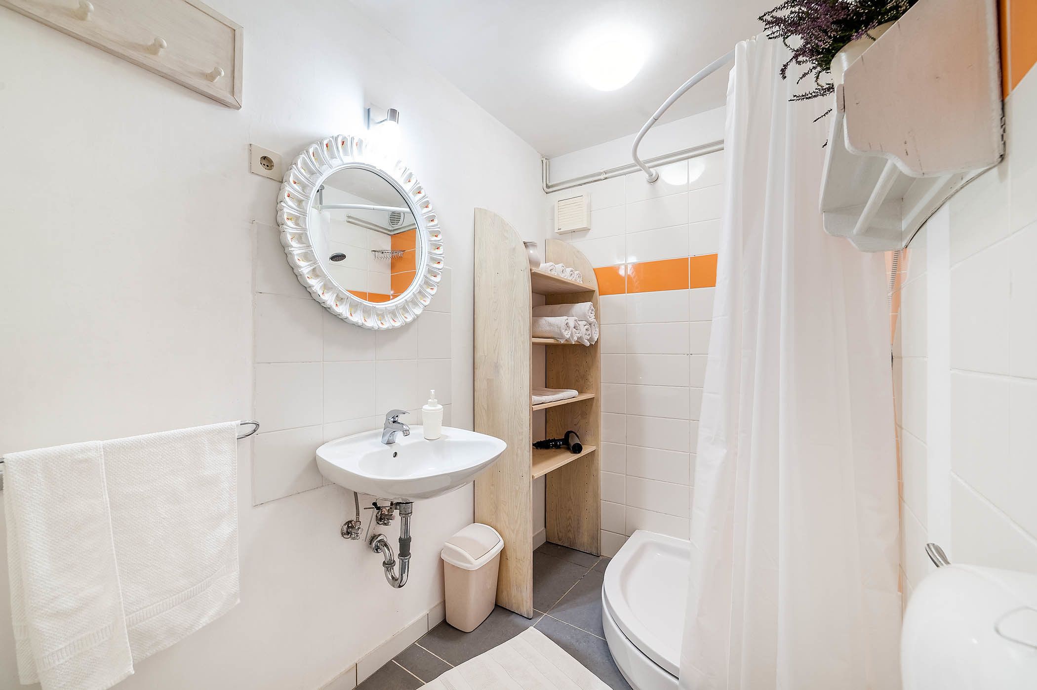 A bathroom with a sink, mirror, towel rack, shower, and a wooden shelf with towels.