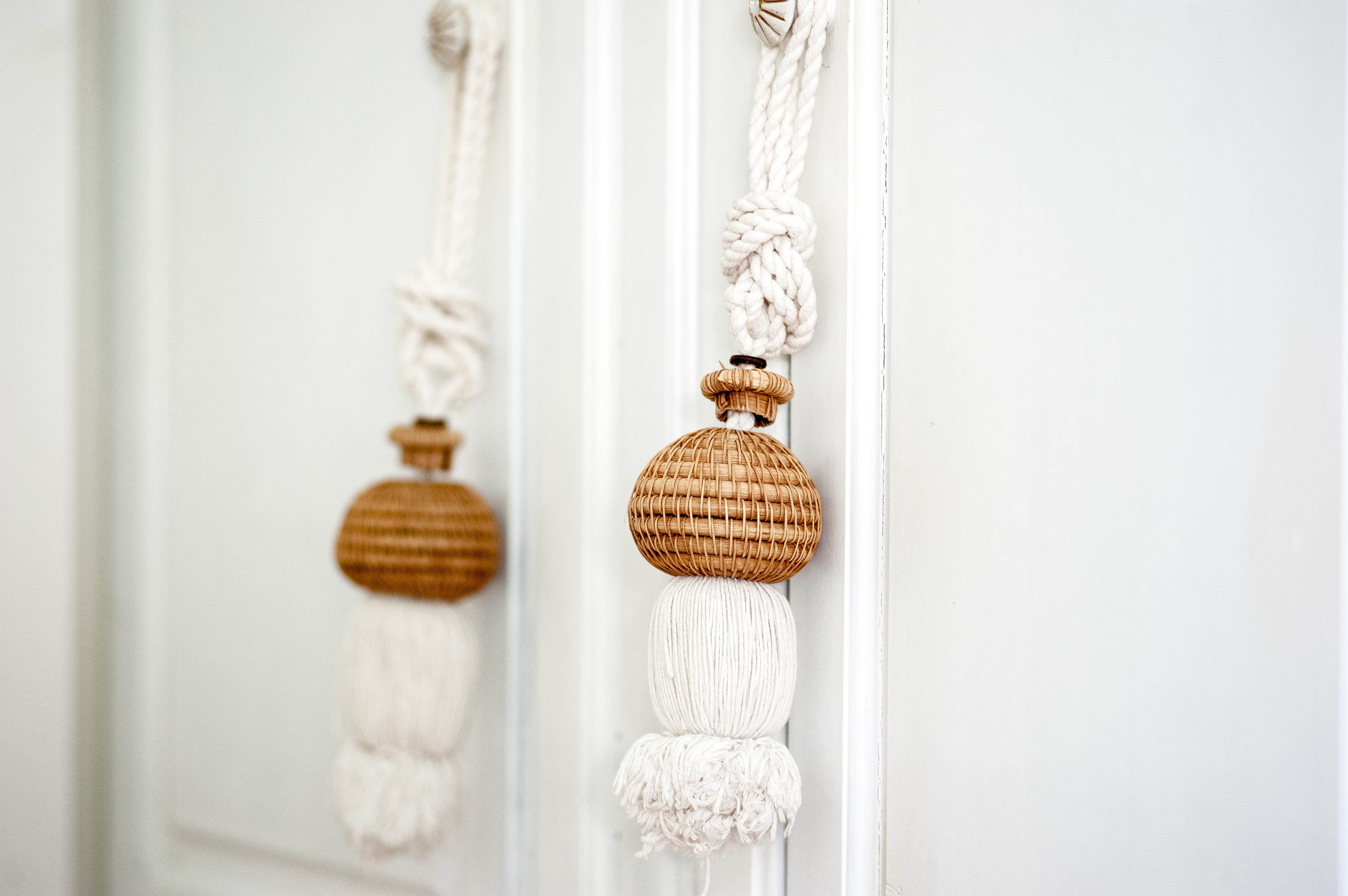 A white door with a macramé decoration featuring a brown spherical object and white tassels.