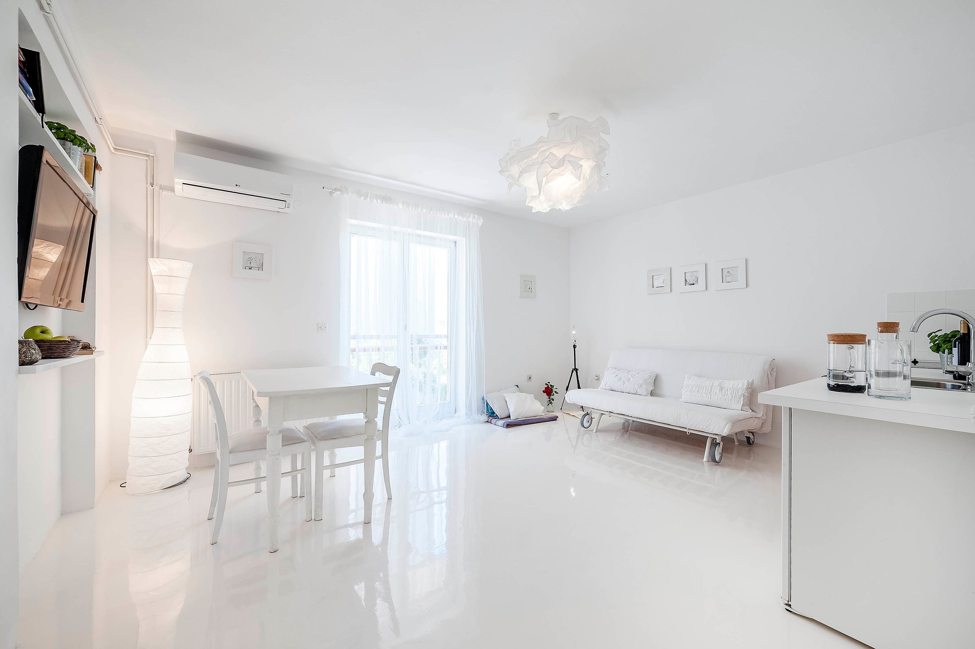 Un salón luminoso y blanco con comedor, sofá y mesa.