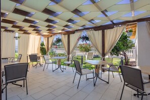 An outdoor patio area with tables and chairs, a pergola with a checkered pattern, and hanging plants. - Bed & Breakfast Maki (Biograd na Moru)