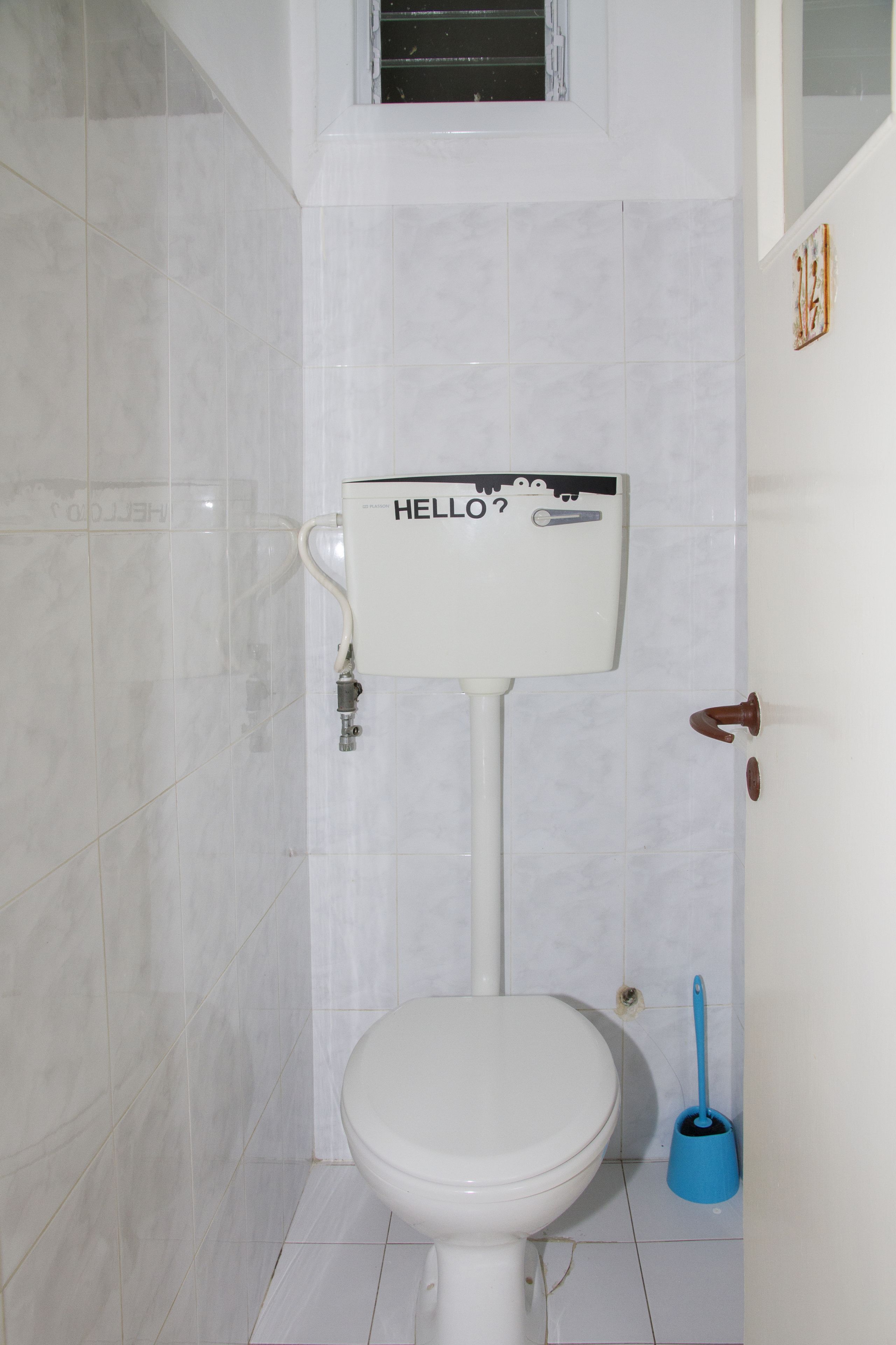 A bathroom with a toilet, a blue plunger, and a wall-mounted toilet paper holder with a cartoon character.