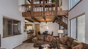 A spacious living room with a high wooden staircase, a large window, and a cozy seating area.