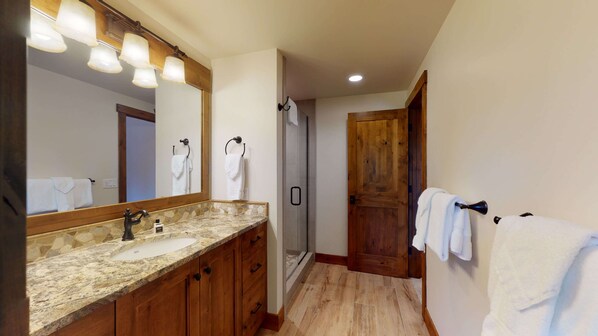 Une salle de bain dotée d’un comptoir en granit, d’un meuble-lavabo en bois, d’un grand miroir et d’un espace douche.