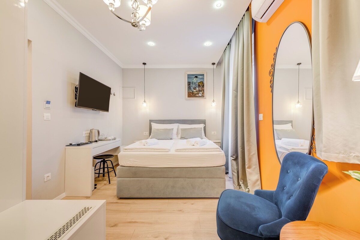 A bedroom with a bed, a desk, a chair, a TV, and a mirror.