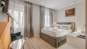 A modern hotel room with a bed, a desk, a chair, and a painting on the wall. - Piano Suites (Split)