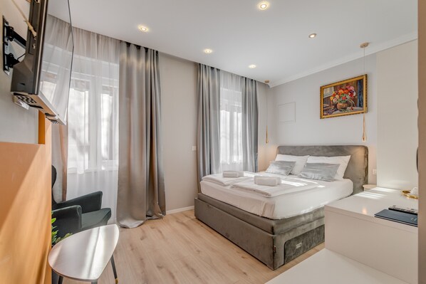 A modern hotel room with a bed, a desk, a chair, and a painting on the wall. - Piano Suites (Split)