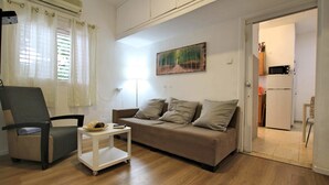 A living room with a sofa, a chair, a small table, and a painting on the wall. - KAV Apartments -Near Assuta Olei Gardom (Tel Aviv)